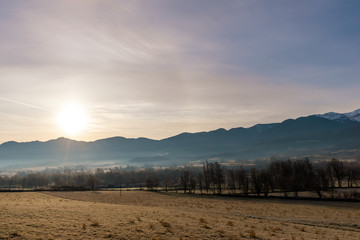 A picturesque landscape view of the hazy snow capped Spanish Pyrenees mountain range in the countryside on an early cold winter morning with the sun behind the clouds