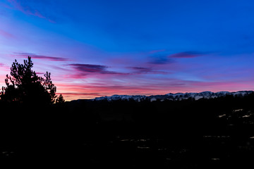 A picturesque landscape view of the silhouette of the Pyrenees mountain range and trees during the sunrise with the sky of vibrant bright colors