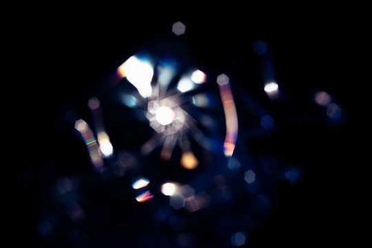 Abstract Shining bokeh lights glass rays on black background. Creative flash lens flare reflection of water, stars, diamond crystal jewelry. Blurred defocused glowing sparkling rainbow colorful light 