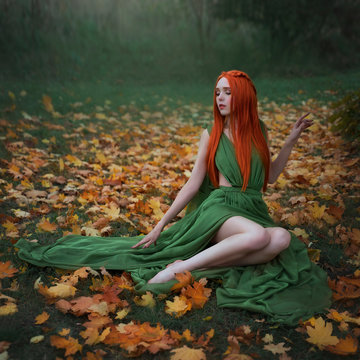 A beautiful long-Haired red-haired elf girl is sitting under a yellow maple tree in the autumn forest. A fairy woman with long hair in a medieval dress.