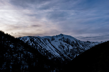 A picturesque landscape view of the snow capped Pyrenees mountain range and the dramatic cloudy sky in the Vall de Sorteny (Andorra) natural park on a cold winter evening during sunset