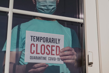 Business owner in medical mask puts a CLOSED sign on the front door due to the coronavirus COVID19...