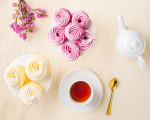 Top view of pink and white marshmallows with tea cup and flowers on white wooden background