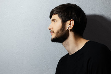 Fototapeta premium Profile portrait of young guy using wireless earphones on background of textured wall of grey.