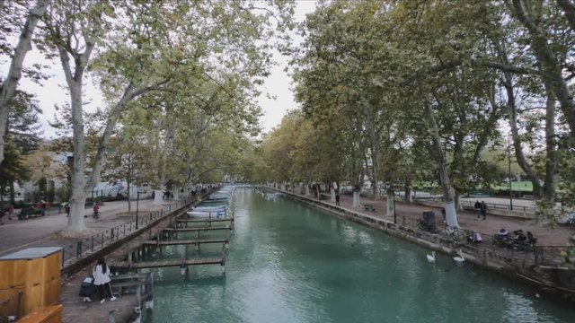 PAN SHOT - Vass&eacute; canal and its moored boats, banks and lines of plane trees in autumn. Canal du Vasse as seen from Pont des Amours, Annecy, France.
