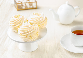 Side view of white marshmallows with tea cup and teapot on white wooden background
