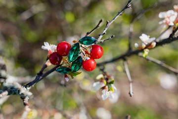 Cute little brooches in the form of red cherries with green leaves made of emerald green stones. In combination with different elements of nature, branches of a flowering Bush with white petals