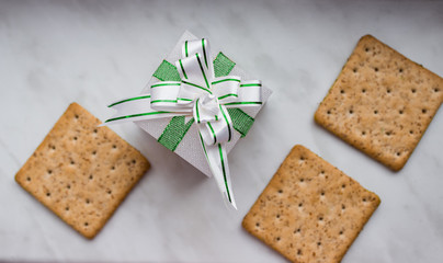 Flat lay. Top view. New Year's gift with bow of green ribbons and lean ruddy crackers with bran on white background