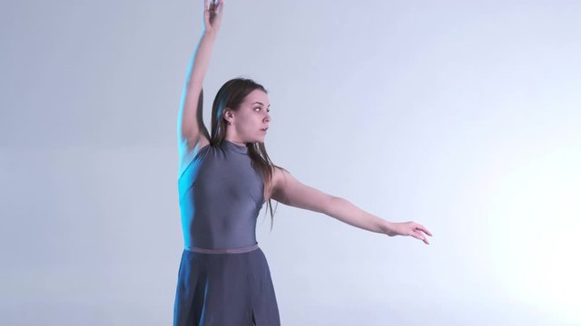 Medium long shot of young beautiful woman dancer in a dress with long hair emotionally dancing contemporary, modern ballet dance in the studio in color back light, slow motion, isolated