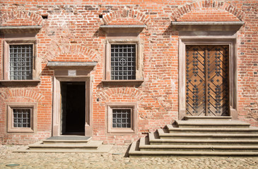 Fototapeta na wymiar wall of an old red brick building with a forged door and four windows on which a patterned protective grille