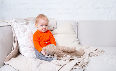 child, baby sitting on a light sofa with a toy in the room