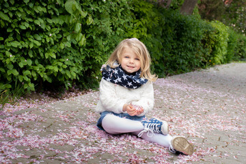 Portrait of a little blonde girl playing with fallen sakura tree flower flower petals
