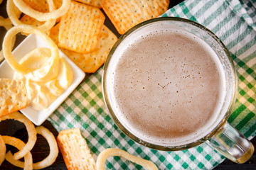  mug of light beer with  onion rings, cracker checkered green towel, top view,