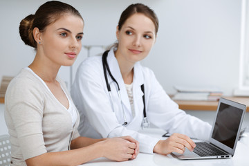 Doctor and patient are sitting and discussing health examination results while using laptop computer. Health care, medicine and good news concepts