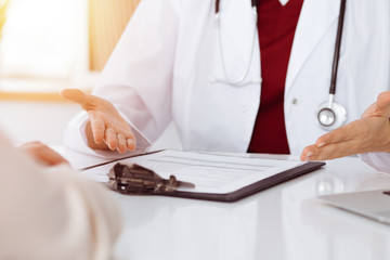 Unknown woman-doctor and patient discussing something while sitting at the table in sunny clinic, close-up