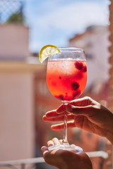 Glass of refreshing summer cocktail on balcony in Europe. Made with berries and citrus fruits