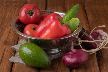 Fresh red tomatoes, bell pepper, cucumbers, red onions and avocado on a wooden background