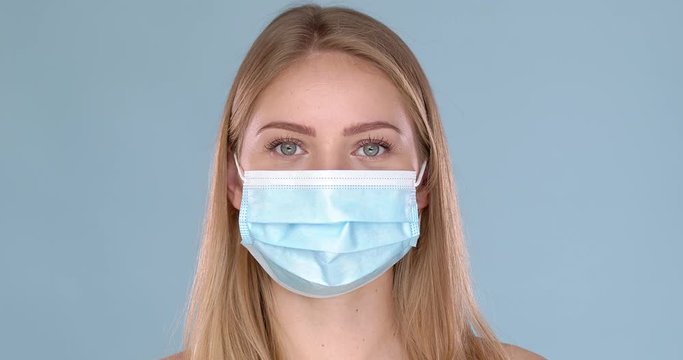 Young woman posing in medical face mask. Looking at camera with smile behind