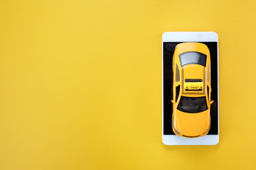 Yellow taxi toy car and smartphone on yellow background with copy space. Top view