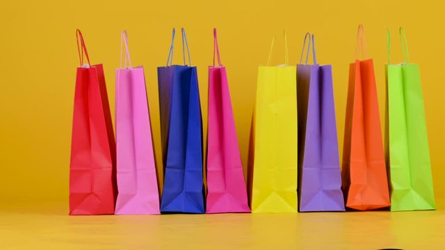 Funny little dog breed Jack Russell Terrier goes on the background of shopping bags on a yellow studio bashound. Shopping concept