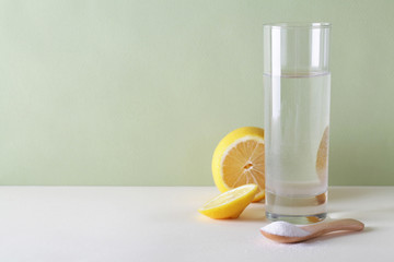 powdered Vitamin C on wooden spoon with glass of water and cut lemon on green and white background