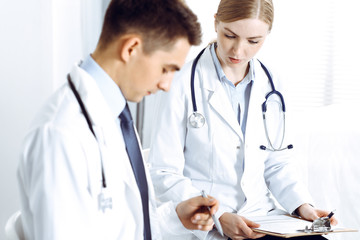 Doctors writing papers using clipboard. Physicians discussing medication program or studying at medical conference. Healthcare, insurance and medicine concept