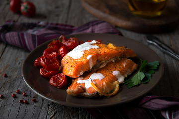 Cooked salmon fish with cherry tomatoes on dark background