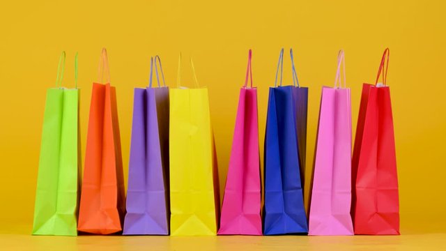 Funny little dog breed Jack Russell Terrier goes on the background of shopping bags on a yellow studio bashound. Shopping concept