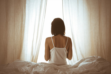 Woman stretching hands in bed after wake up, sun flare . Brunette entering a day happy and relaxed after good night sleep and back view. Concept of a new day and joyful weekend