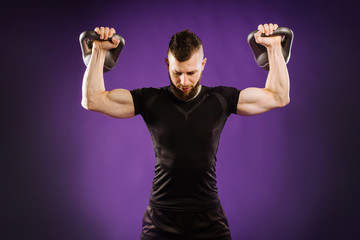 Fototapeta na wymiar Young muscular man doing exercises with weight on purple studio background. Copy space