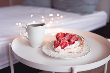 Tasty  homemade cake with fresh strawberry on white plate with cup of coffee on table in room closeup. Good morning.