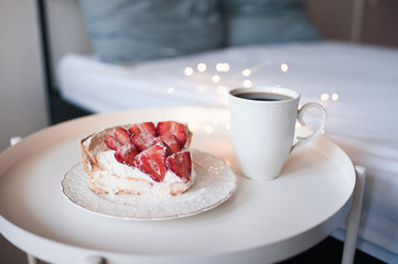 Cup of fresh coffee with unbaked strawberry cake on table in room over glowing light at back. Good morning. Birthday surprise.