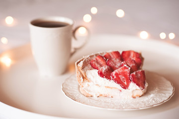 Strawberry cake with fresh fruit on top staying on white plate with cup of fresh coffee on table closeup. Good morning. Breakfast time. Birthday party.