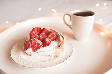 Strawberry cake with fresh fruit on top staying on white plate with cup of fresh coffee on table closeup. Good morning. Breakfast time. Birthday party.