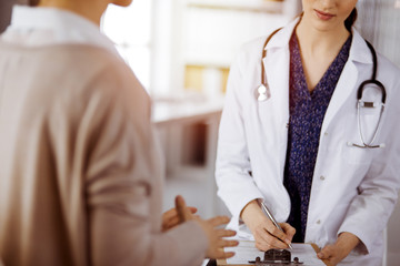 Doctor and patient discussing current health examination while sitting in sunny clinic. Perfect...
