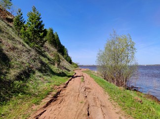 The road along the river bank near the slope with green trees against the blue sky
