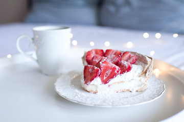 Tasty unbaked homemade cake with fresh fruits and mug of tea at back with glowing lights closeup. Good morning. Birthday party.