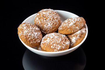 Appetizing oatmeal cookies sprinkled with icing sugar in a white plate close-up on a black mirror background. Horizontal orientation. 
