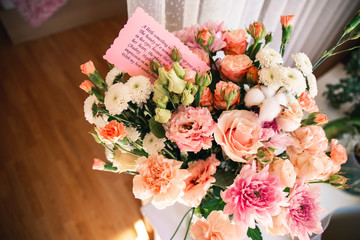 Beautiful bright bouquet of flowers with a note in the morning bedroom. 