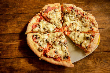 pizza cooked at home-made is cut into pieces and lies on a wooden table