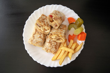Famous traditional Arabic, Middle East, Israel cuisine. Arabic chicken shawarma plate with fried fries and pickled vegetables on dark wooden background, top view. Shawarma wrap on white plate 