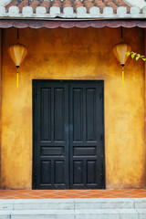 a beautiful black wooden door on a yellow wall with Chinese lanterns.Ancient city of Hoi an. Vietnam.