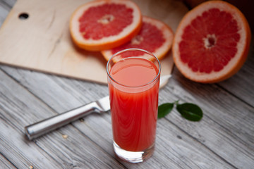grapefruit juice in a glass glass and cut grapefruit and knife on a light  wooden background