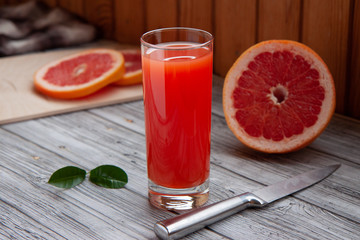 grapefruit juice in a glass glass and cut grapefruit and knife on a light  wooden background