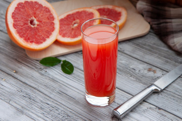 Fototapeta na wymiar grapefruit juice in a glass glass and cut grapefruit and knife on a light wooden background
