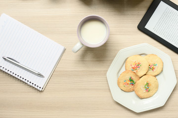 Vista de cima de uma mesa com uma xícara com leite e biscoitos simples com confeitos coloridos,...