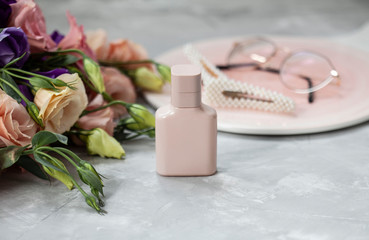 Pink perfume bottle with flowers and pink fashionable accesories on grey background