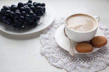 Coffee break with cookies and bunch of purple grapes served on white dresser scarf and white background  