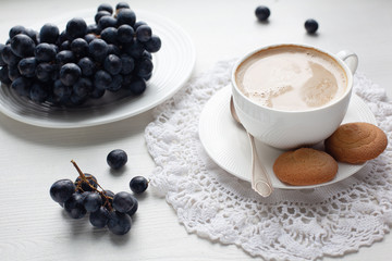 Coffee break with cookies and bunch of purple grapes served on white dresser scarf . White background  .