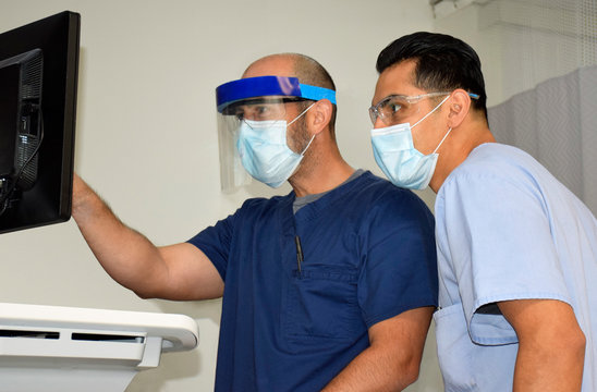 Masked Doctors At Computer With Protective Equipment